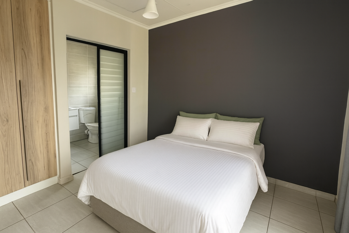A well-maintained bedroom featuring a built-in wardrobe, tiled flooring, and an adjoining en-suite bathroom with a sliding door entry.