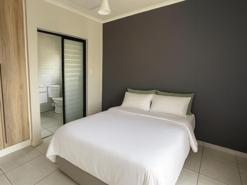 A well-maintained bedroom featuring a built-in wardrobe, tiled flooring, and an adjoining en-suite bathroom with a sliding door entry.