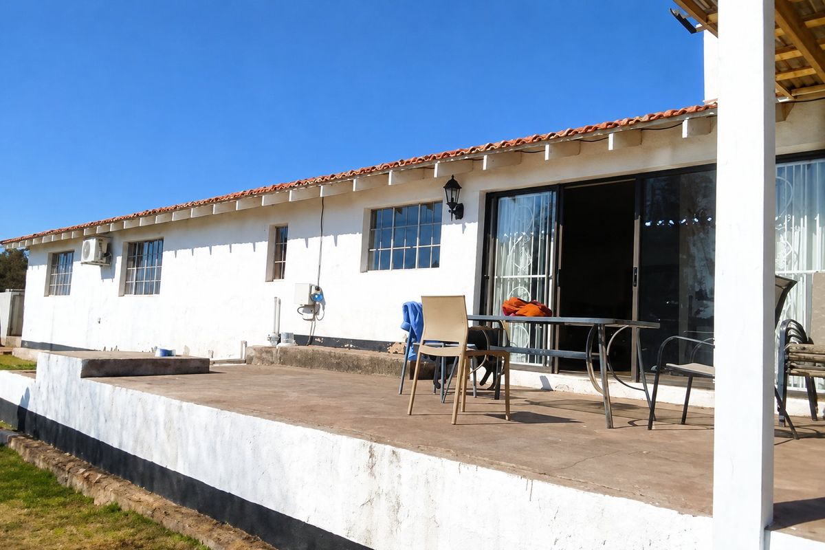Rear elevation of a farm-style dwelling featuring a concrete patio, sliding glass doors, and terracotta roof tiles, showing signs of exterior wear.