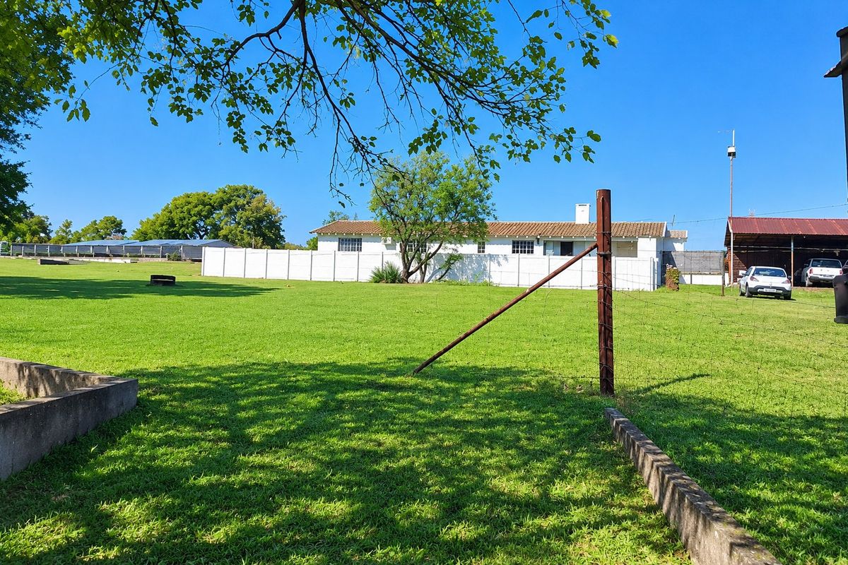 A spacious, well-maintained lawn area on a farm property, featuring perimeter fencing, concrete curbing, and a view of the main dwelling and outbuildings.