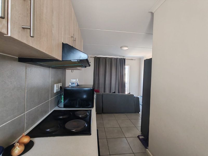 Open-plan kitchen and living area featuring modern cabinetry, electric hob, extractor fan, and neutral tiled flooring throughout the space.