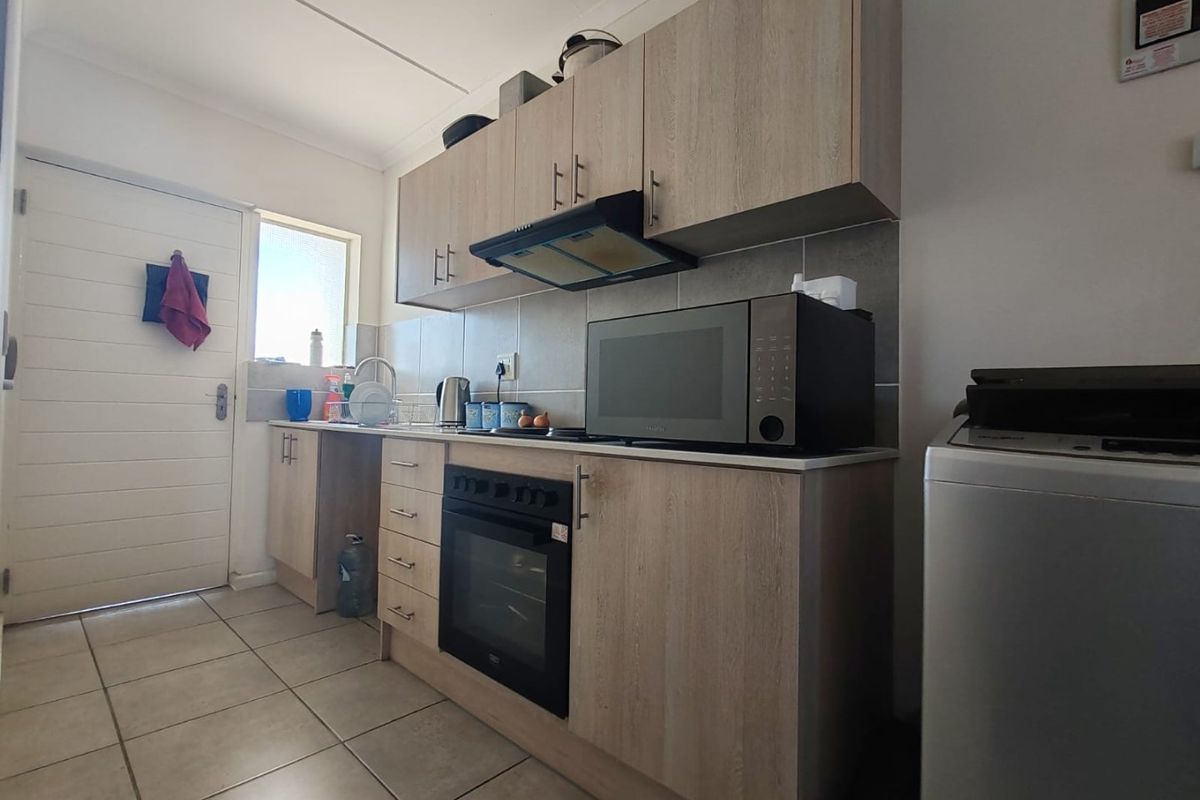 A functional kitchen featuring light wood-grain cabinetry, built-in oven and hob, extractor fan, and tiled flooring with a neutral backsplash.