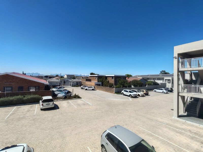 An elevated view overlooking a paved parking area and surrounding residential neighborhood with mountain views in the distance.