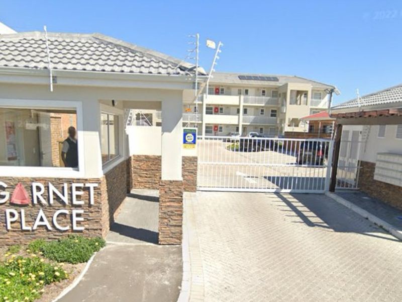 The entrance to Garnet Place apartment complex featuring a secure gated access point, guard house, and paved driveway.