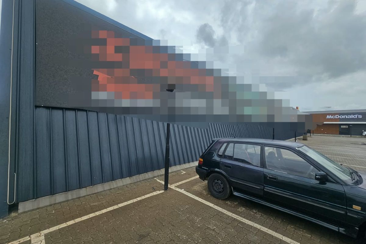 Exterior view of a commercial building featuring metal cladding, a paved parking area, and a large digital billboard.