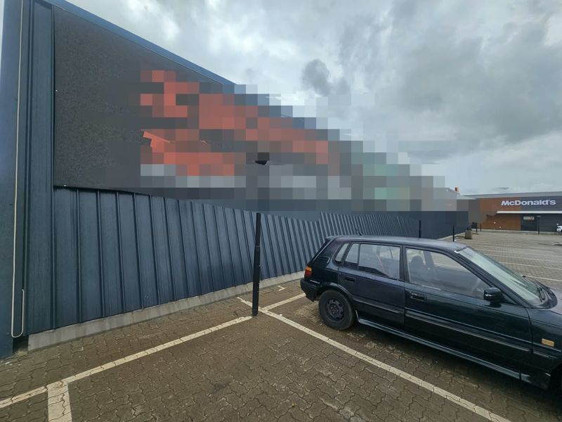 Exterior view of a commercial building featuring metal cladding, a paved parking area, and a large digital billboard.