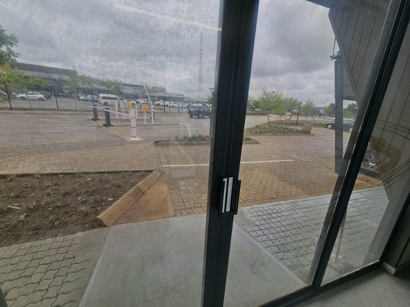View from inside looking out through a sliding glass door towards the paved parking area and commercial exterior.