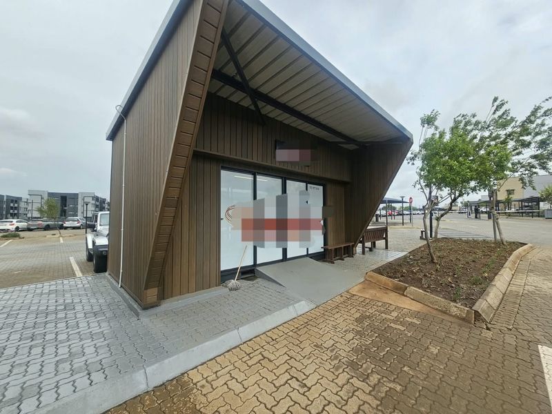Modern commercial unit featuring timber cladding, a prominent metal roof overhang, glass storefront entrance, and an accessible concrete ramp.