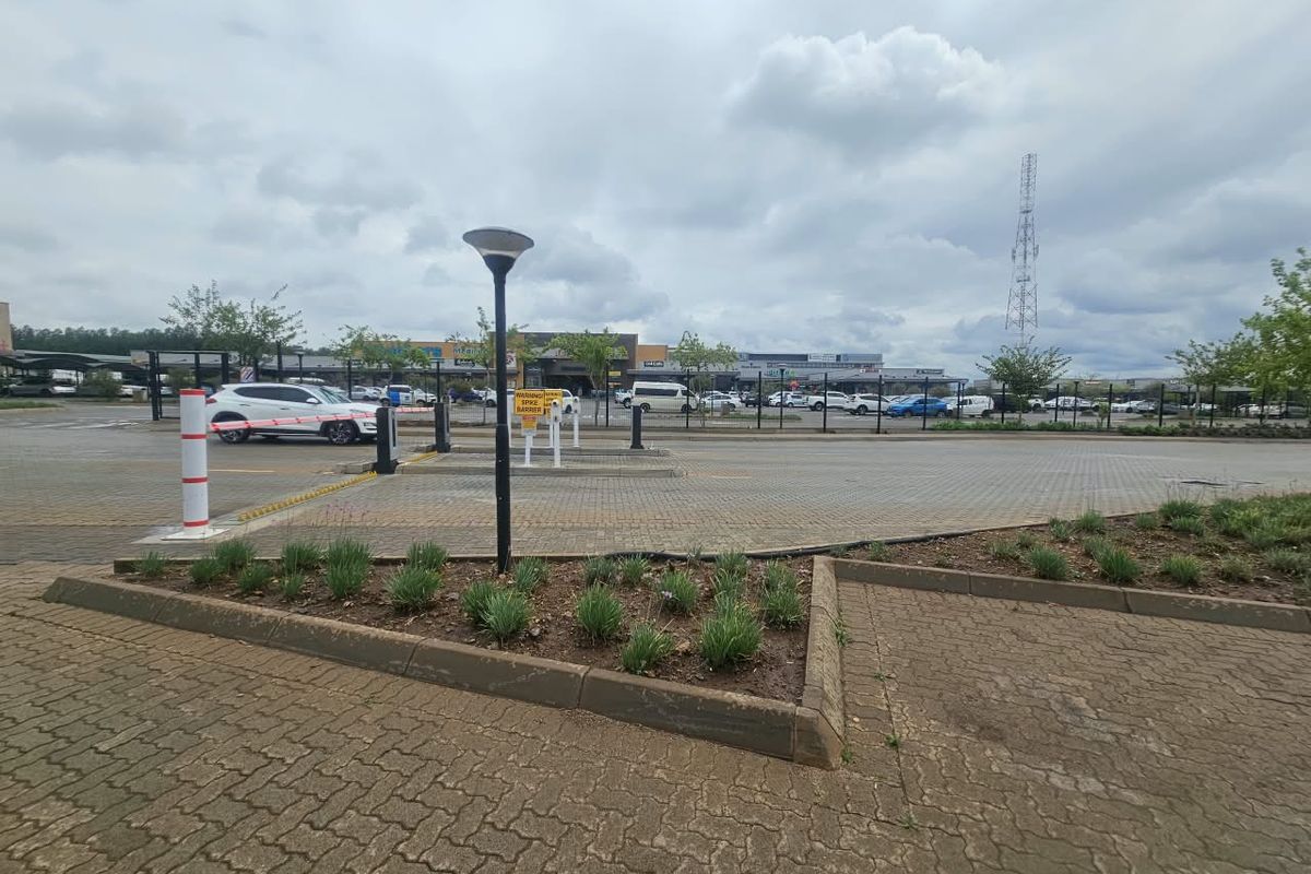 Commercial property entrance featuring a paved driveway, security boom gate with spike barrier, and landscaped garden beds.