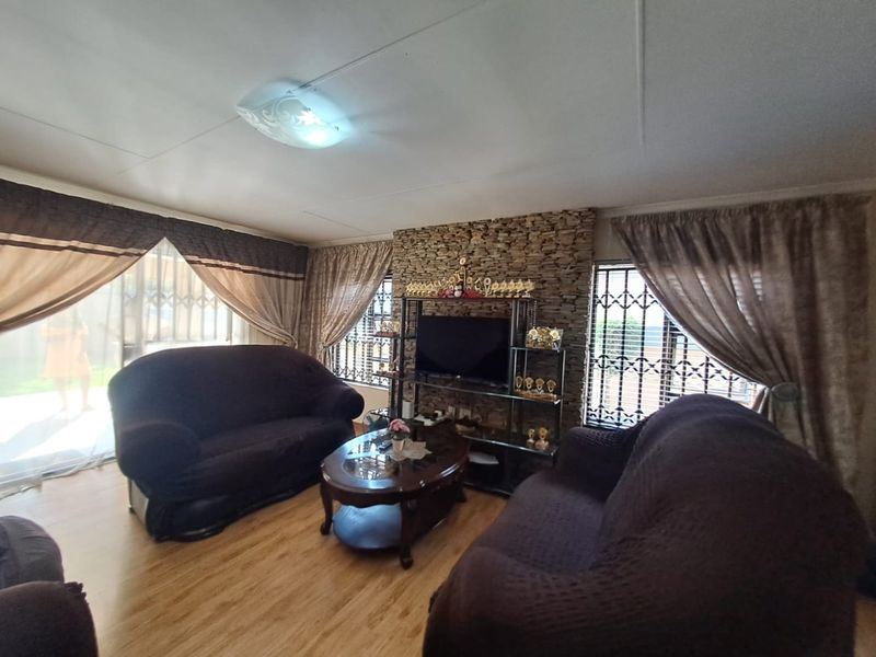 A living room featuring a stone accent wall, laminate flooring, and large windows with security bars, providing a functional and cozy living space.