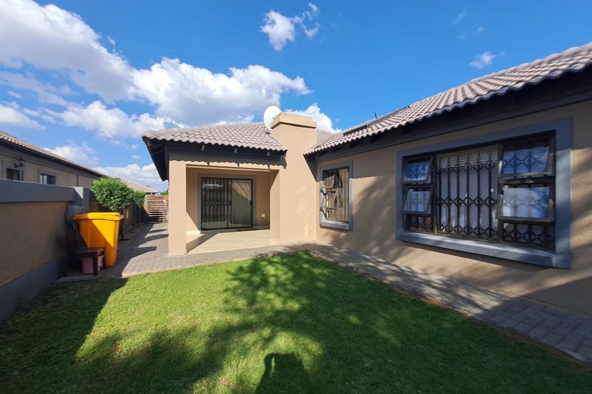 Rear view of the property featuring a covered patio, paved walkway, and a well-maintained lawn area.