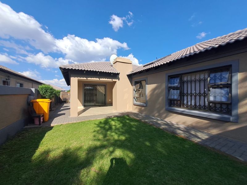 Rear view of the property featuring a covered patio, paved walkway, and a well-maintained lawn area.