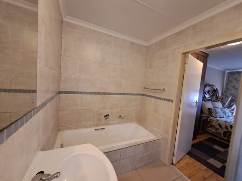 A functional bathroom featuring a built-in bathtub, wall-mounted basin, and neutral tiled finishes, providing a clean and practical space.