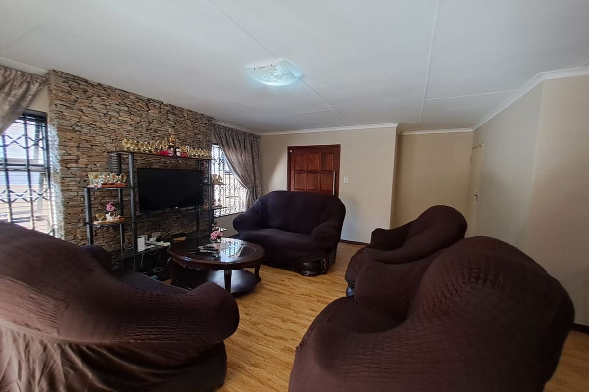 A living room featuring a textured stone accent wall, laminate flooring, and security bars on the windows.