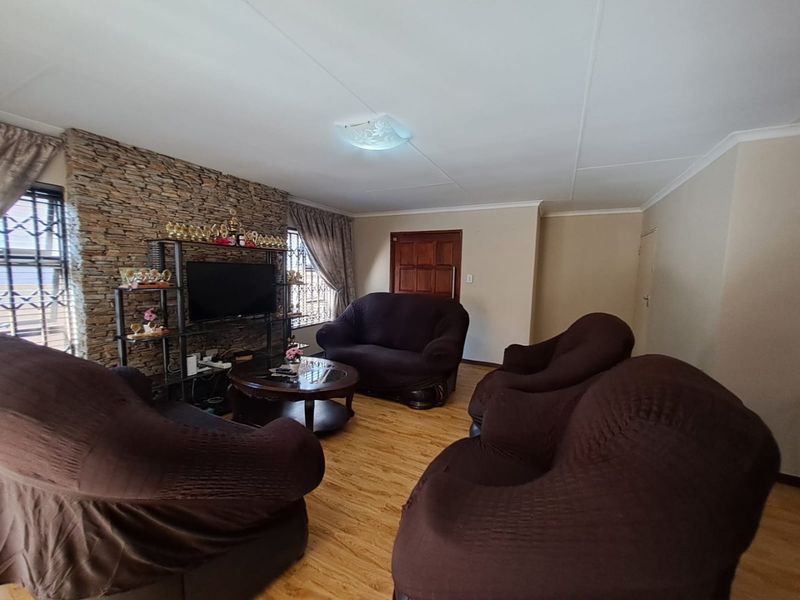 A living room featuring a textured stone accent wall, laminate flooring, and security bars on the windows.