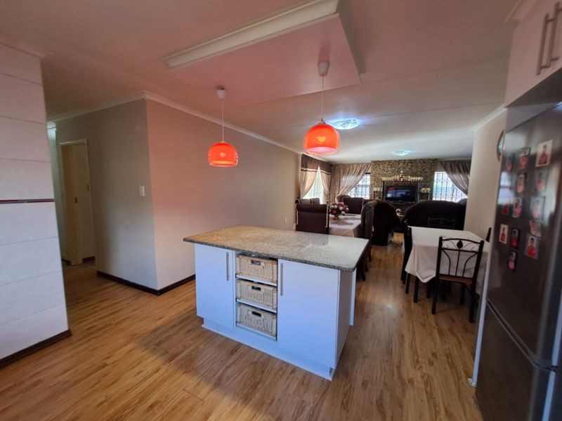 Open plan living and dining area featuring a central kitchen island with granite countertop, pendant lighting, and a stone feature wall in the lounge.