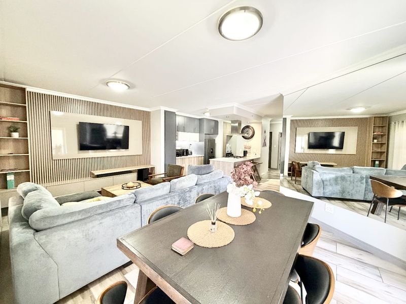 Modern open-plan living and dining area featuring a stylish slatted timber feature wall, contemporary kitchen with island, and large mirrored wall enhancing the space.