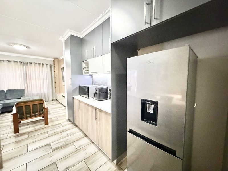 Modern open-plan kitchen featuring sleek two-tone cabinetry, tiled flooring, and integrated storage, seamlessly flowing into the adjacent living area.