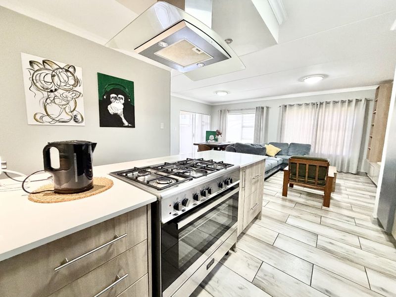 Open-plan living area featuring a modern kitchen with gas stove, extractor fan, and stone countertops, flowing into a spacious lounge and dining space.