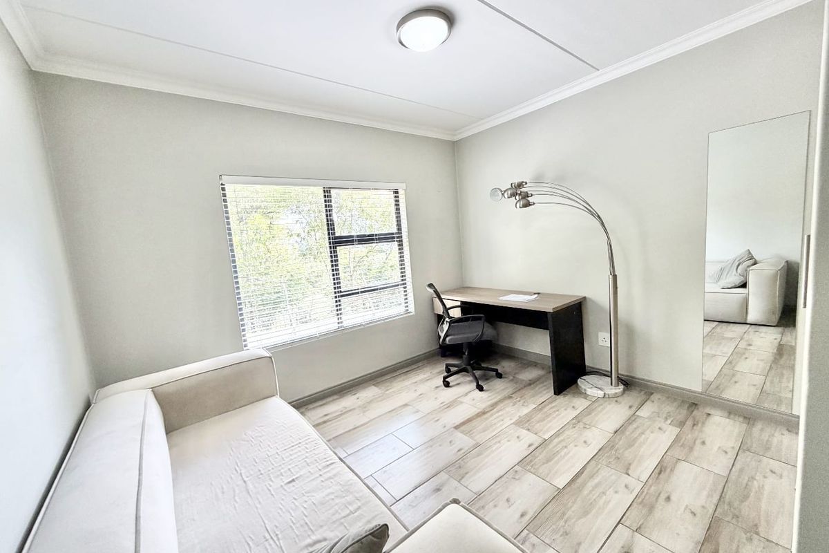A bright bedroom featuring light-toned tiled flooring, a large built-in mirror, and an aluminium-framed window with venetian blinds.