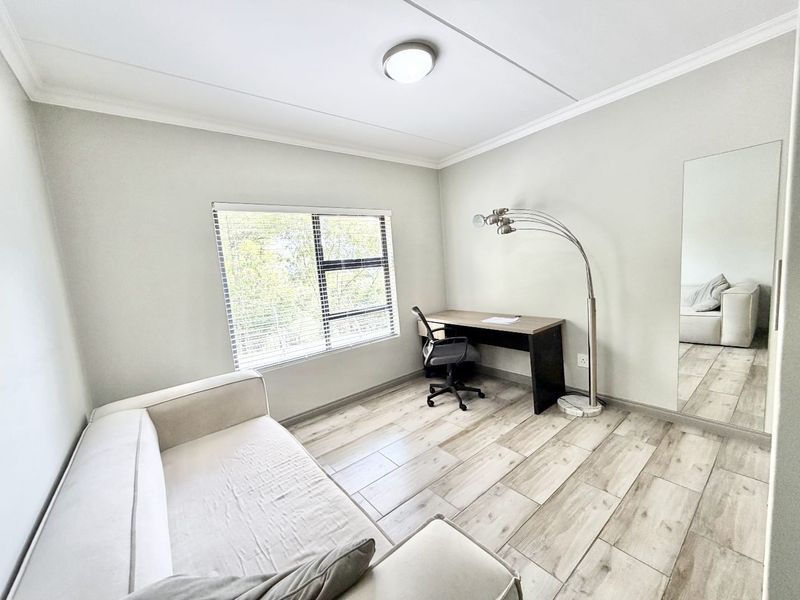 A bright bedroom featuring light-toned tiled flooring, a large built-in mirror, and an aluminium-framed window with venetian blinds.