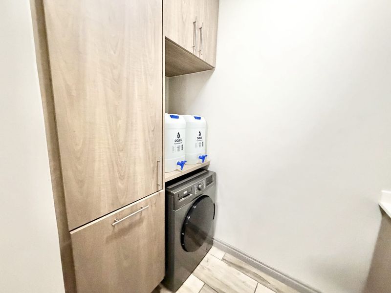 A compact laundry area featuring modern light wood-toned built-in cabinetry and tiled flooring, providing efficient storage and utility space.