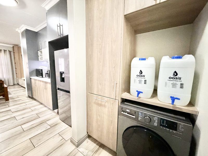 A modern scullery area featuring light wood-finish cabinetry, integrated appliance space, and durable tiled flooring, providing functional utility and storage adjacent to the kitchen.