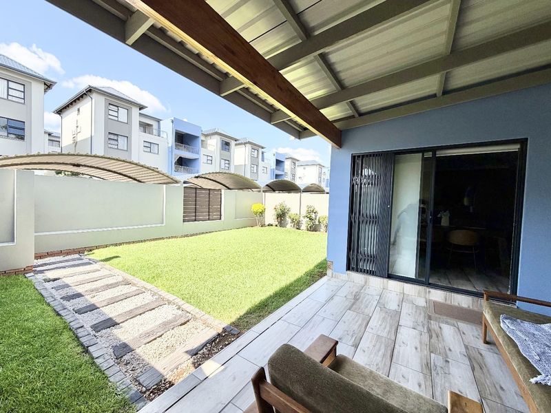 A covered patio area featuring tiled flooring and a sliding glass door, overlooking a well-maintained private garden with a paved walkway.