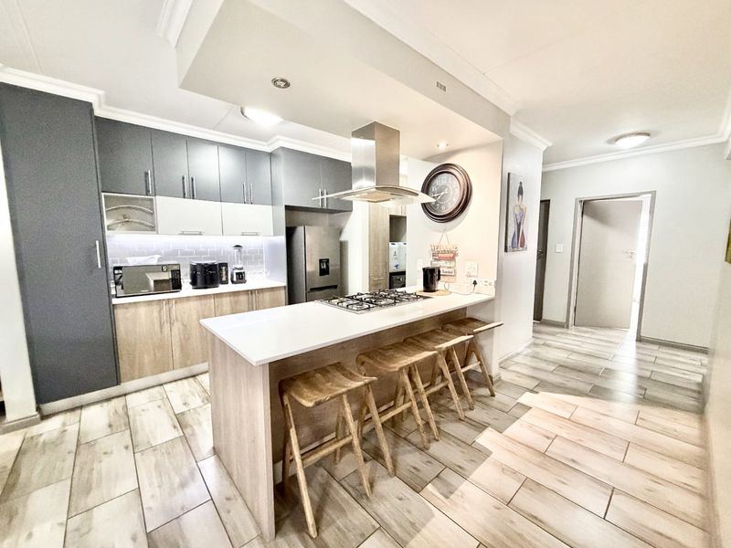 Modern kitchen featuring two-tone cabinetry, stone countertops, a central breakfast island with a gas hob, and integrated extractor fan.