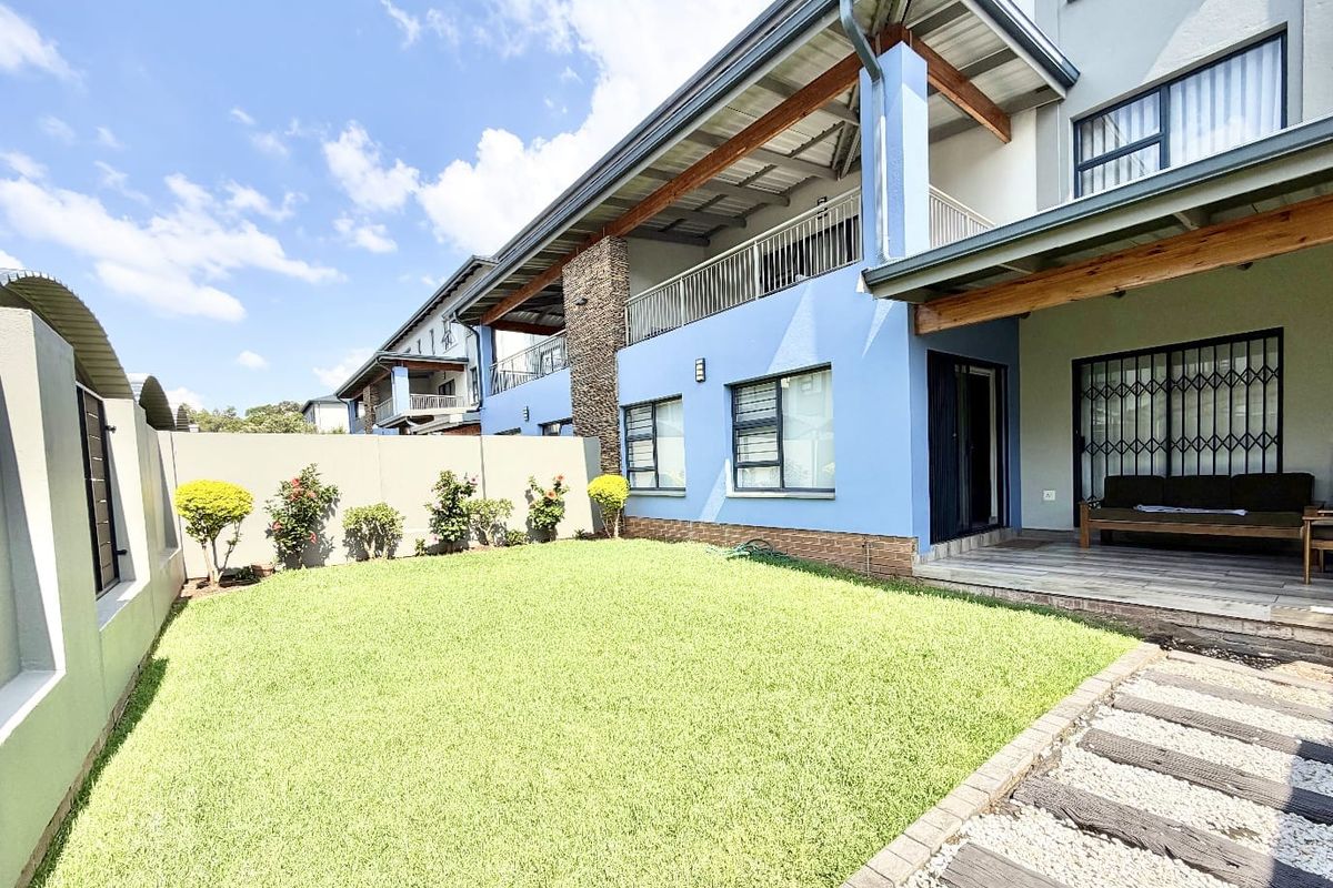 A well-maintained rear garden featuring a covered patio with timber beams, stone cladding accents, and a paved walkway leading to the residence.