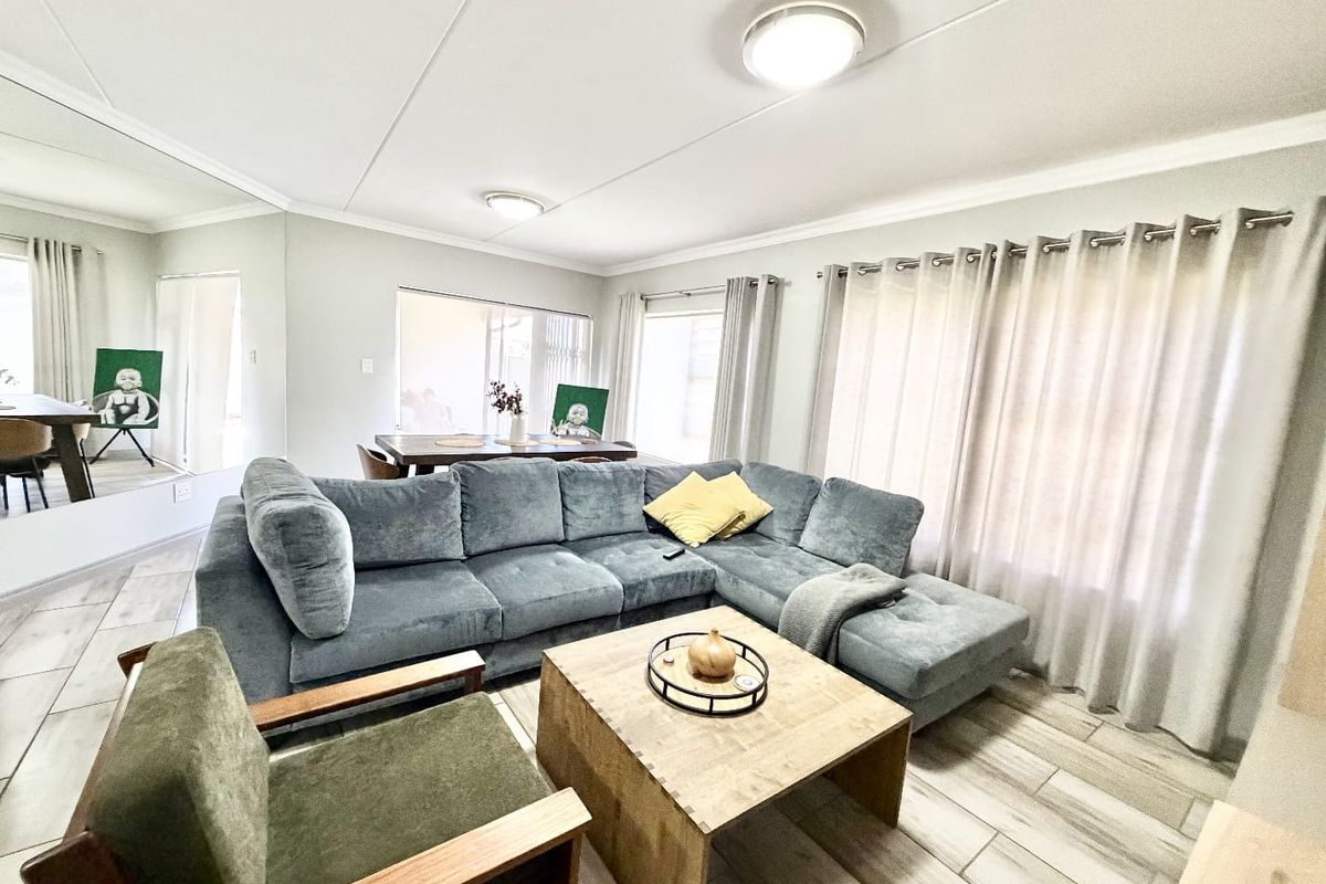 A bright and spacious living area featuring modern tiled flooring, a large mirrored wall, and neutral finishes, creating a comfortable and inviting atmosphere.