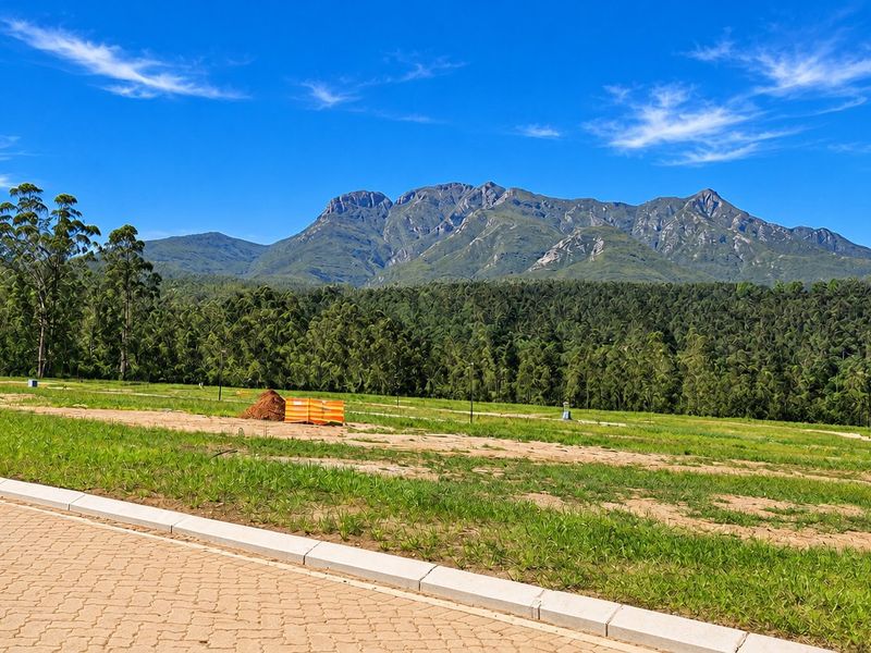 A scenic view of a mountain range overlooking a vacant residential plot with paved road access and concrete curbing.
