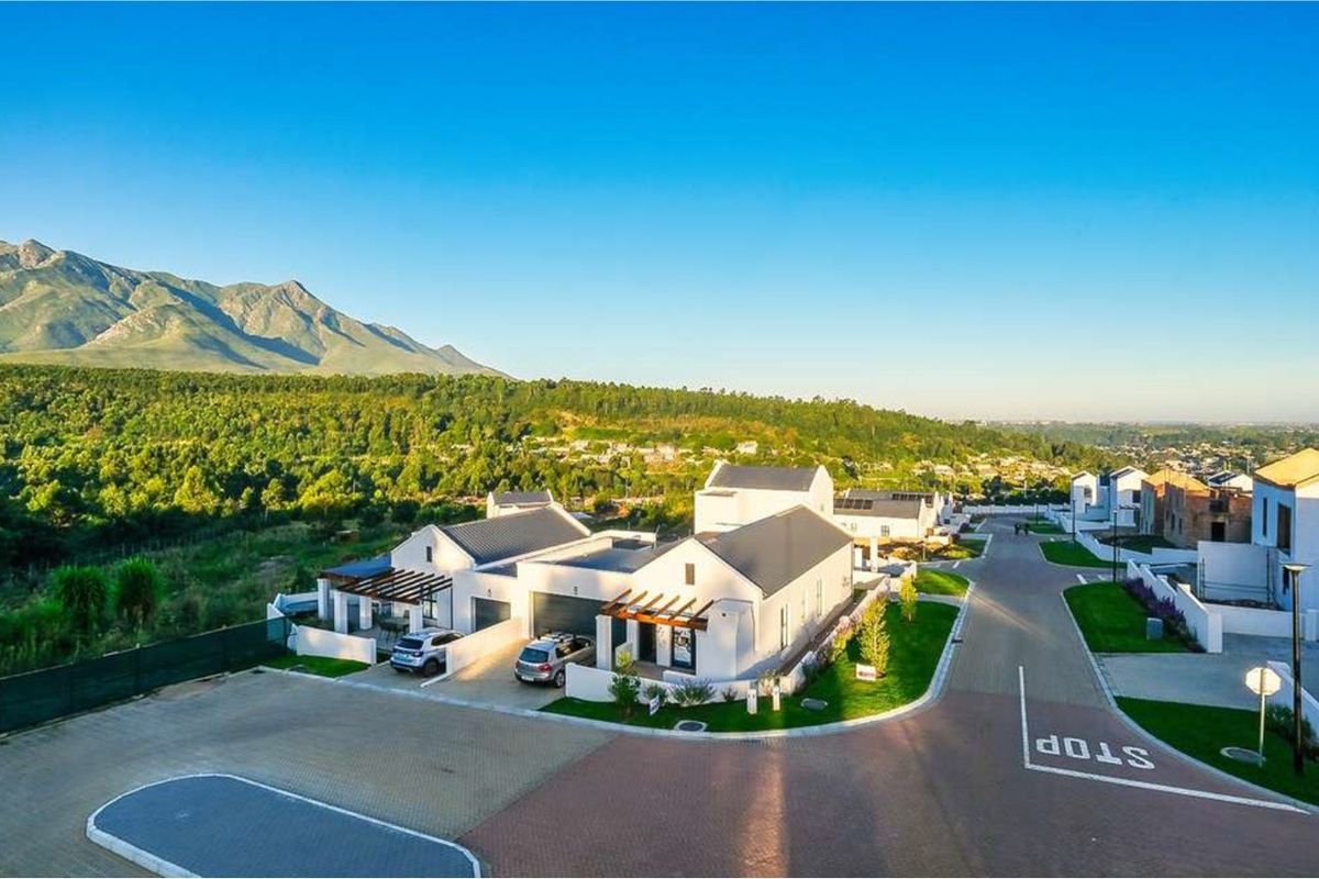 Aerial view of a modern residential estate featuring contemporary homes with pitched roofs, timber pergolas, and paved driveways set against a scenic mountain backdrop.