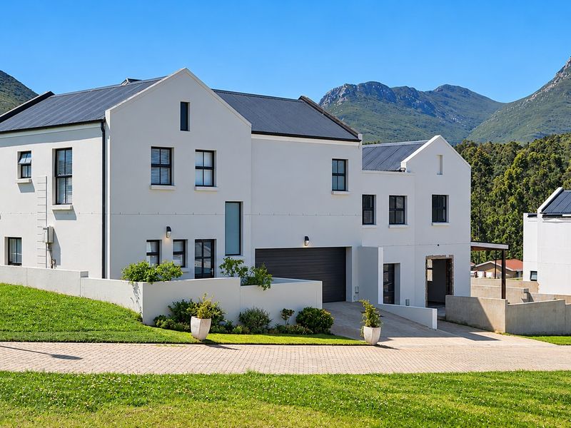 Modern two-story house with a clean white facade, dark metal roof, and integrated garage, set against a scenic mountain backdrop.