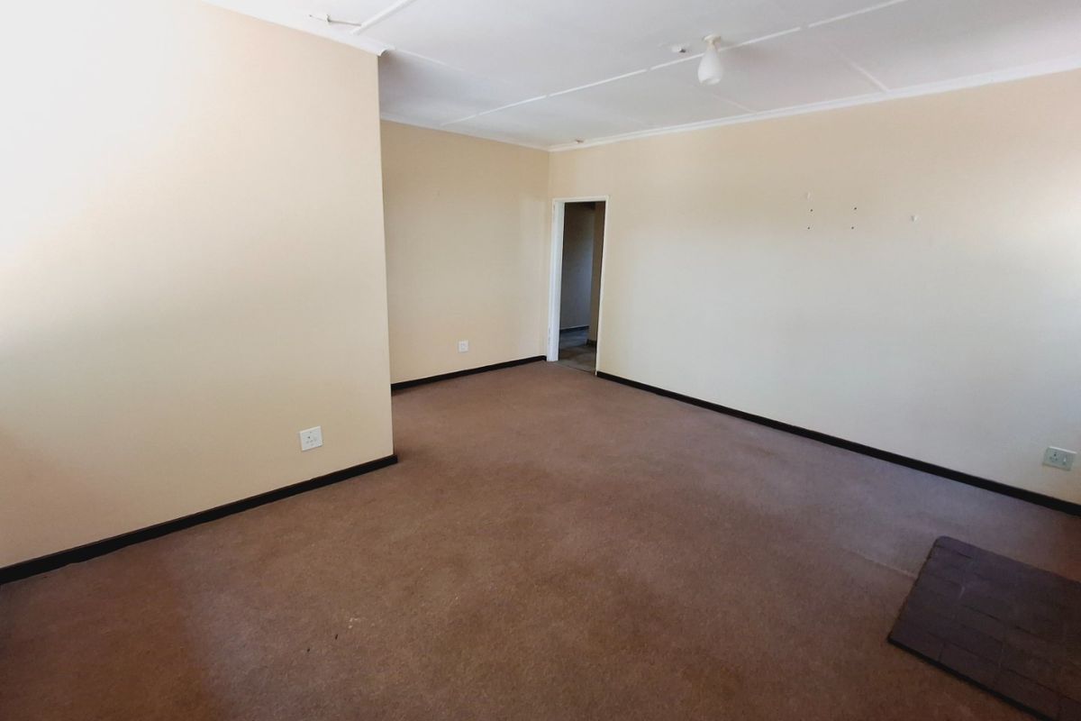 An empty living room featuring carpet flooring, a tiled hearth, and neutral wall finishes, offering a blank canvas for renovation or interior design.