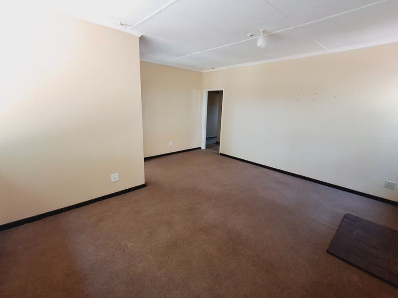 An empty living room featuring carpet flooring, a tiled hearth, and neutral wall finishes, offering a blank canvas for renovation or interior design.