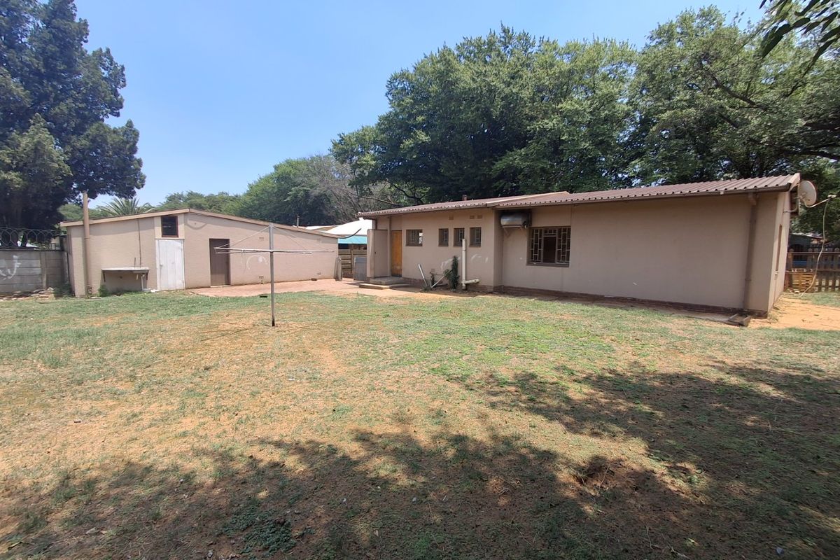 Rear view of the property showing a large backyard, main house structure, and a detached outbuilding with a metal roof.