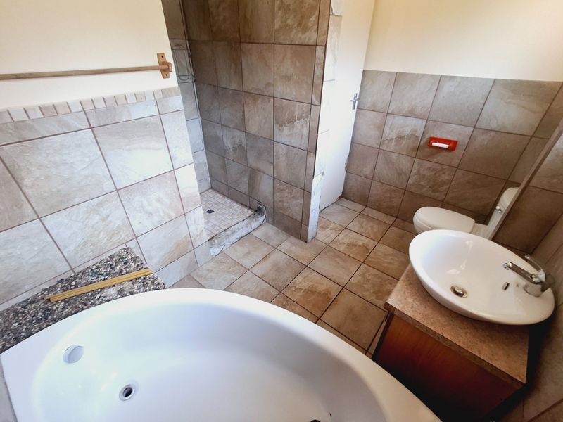 A functional bathroom featuring a built-in bathtub, separate walk-in shower, vanity basin, and toilet with neutral wall and floor tiling.