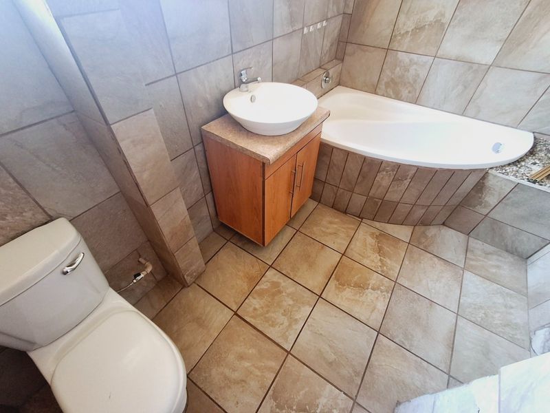 A functional bathroom featuring floor-to-ceiling ceramic tiling, a built-in vanity with a vessel sink, and a tiled bathtub surround.