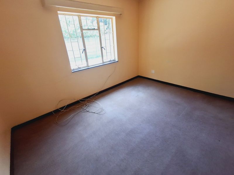 An empty bedroom featuring carpet flooring, security bars on the window, and visible wall plaster cracking, offering a blank canvas for renovation.