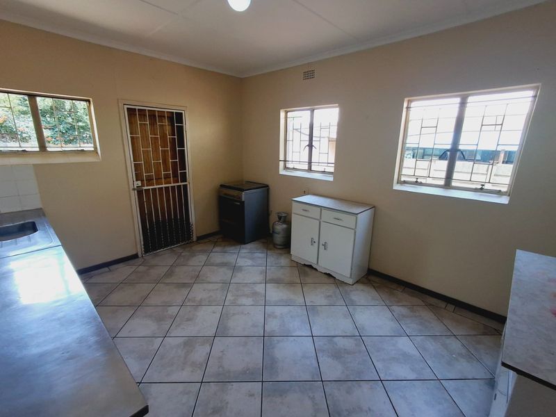 A functional kitchen space featuring tiled flooring, built-in cabinetry, and security bars on the windows, offering a blank canvas for potential renovation.