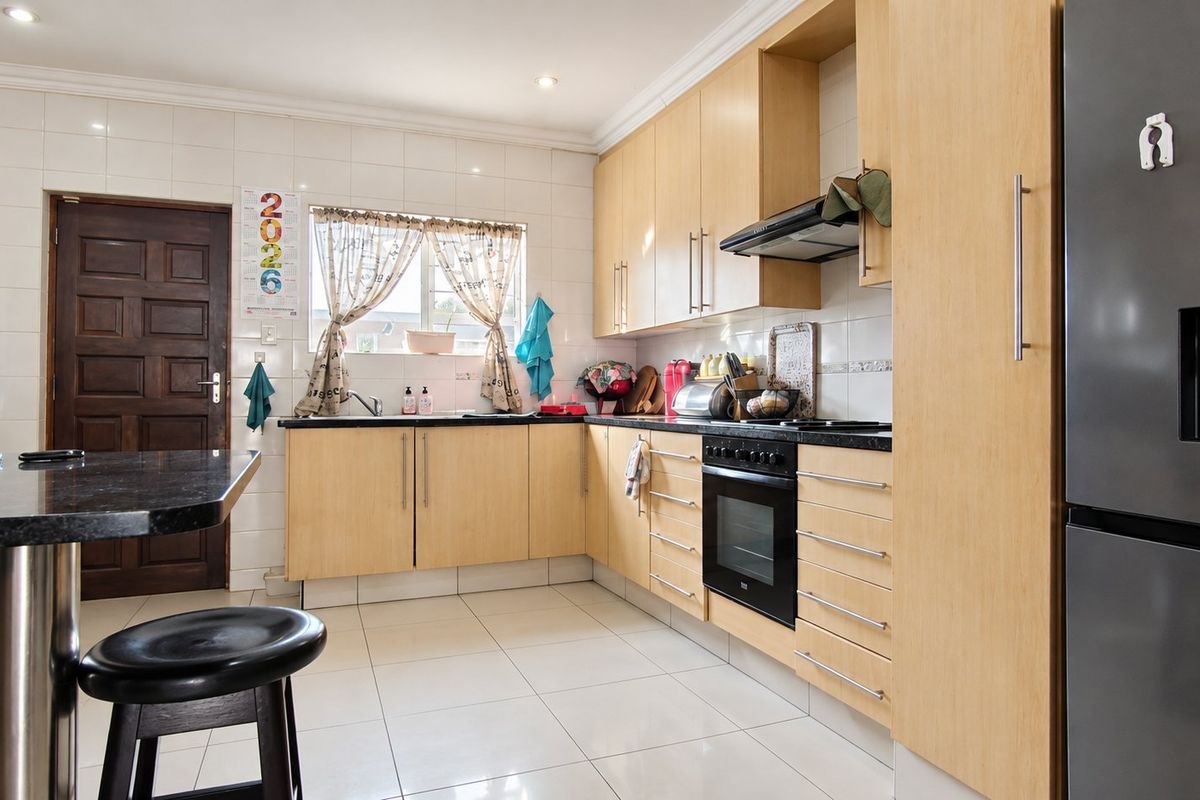 A functional kitchen featuring light wood cabinetry, granite countertops, a built-in oven with extractor fan, and tiled flooring throughout.