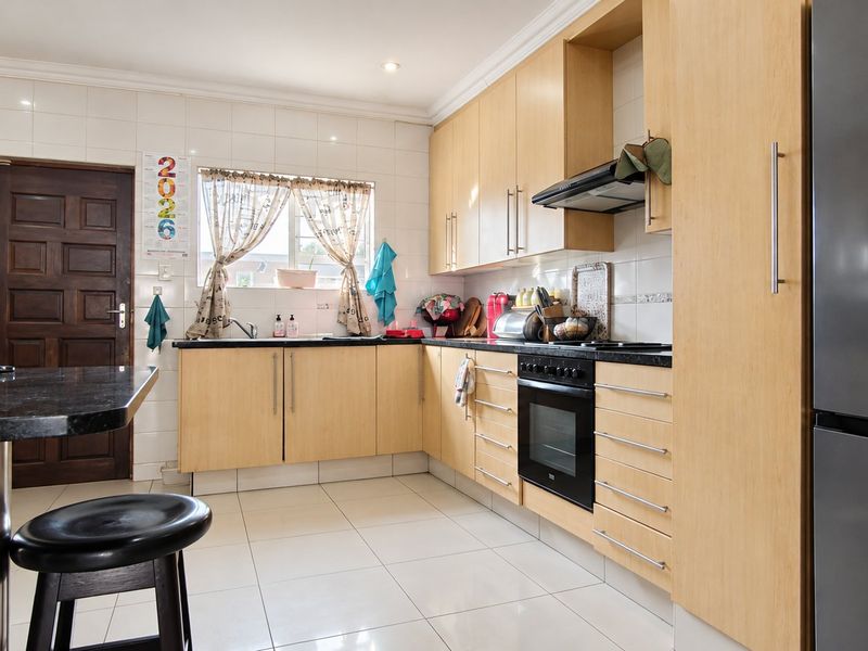 A functional kitchen featuring light wood cabinetry, granite countertops, a built-in oven with extractor fan, and tiled flooring throughout.
