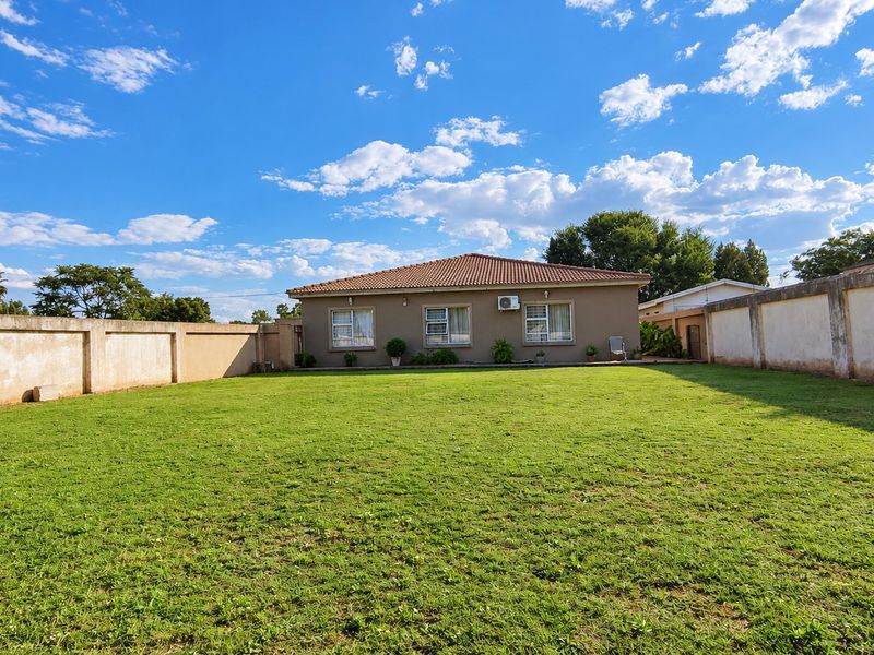 Spacious rear garden featuring a large lawn area, enclosed by high perimeter boundary walls, with a view of the rear house elevation.