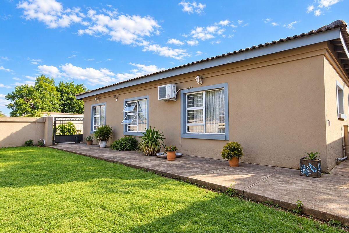Rear view of the property featuring a concrete patio, well-maintained lawn, perimeter wall, and secure gated access.