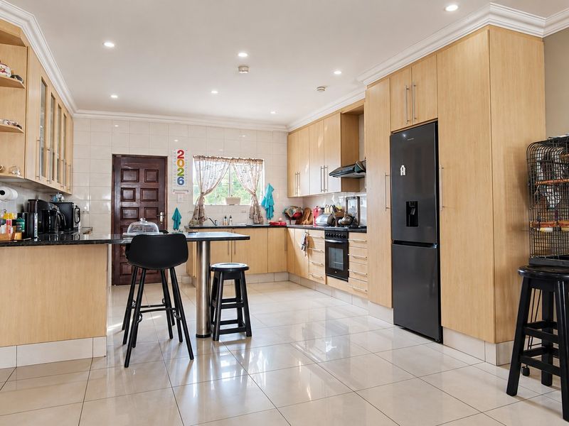 Spacious kitchen featuring light wood cabinetry, granite countertops, integrated oven, extractor fan, and tiled flooring with a breakfast bar area.