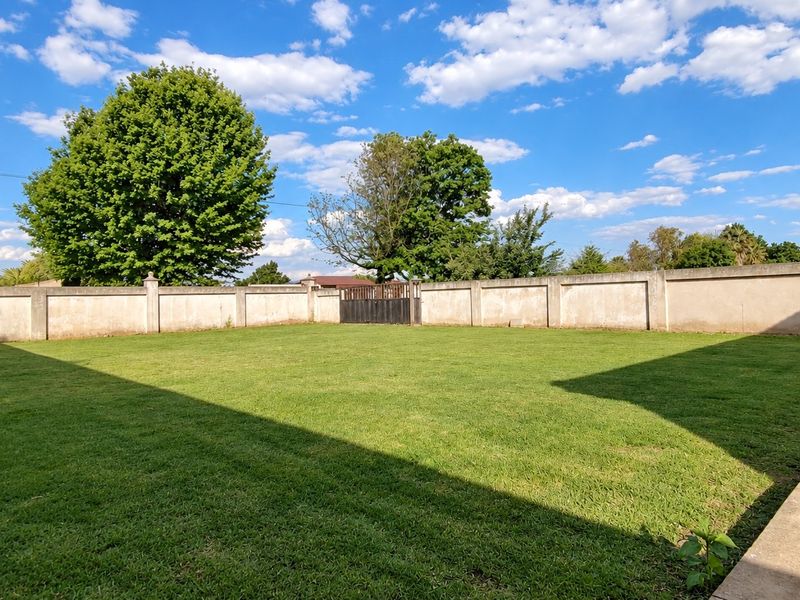 A spacious, well-maintained level lawn area enclosed by a high perimeter boundary wall with a rear access gate.