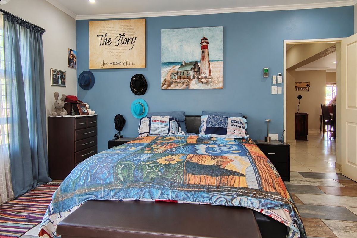 A well-maintained bedroom featuring tiled flooring, an air conditioning unit, and a blue accent wall, with an adjacent view into another living space.