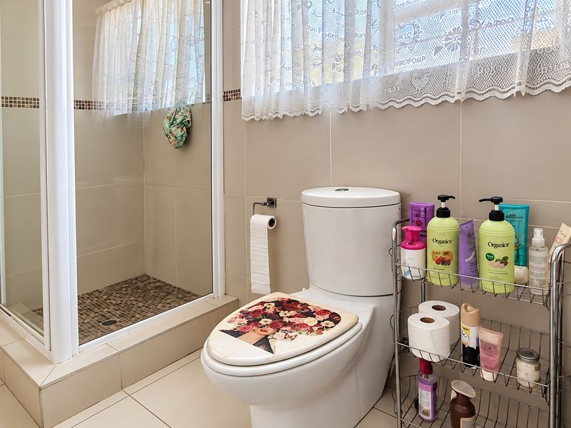 A functional bathroom featuring a tiled shower enclosure, a modern toilet, and neutral wall tiling with a decorative mosaic border.