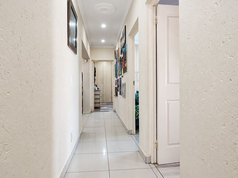 A well-lit hallway featuring neutral textured walls, polished floor tiles, and access to multiple rooms through panel doors.